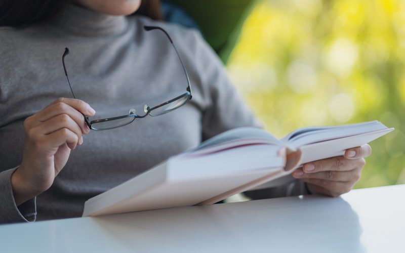 Reader holding an open book and a pair of glasses
